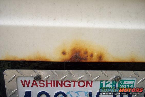 Close-up of rust on a white vehicle panel above a Washington license plate from 2014