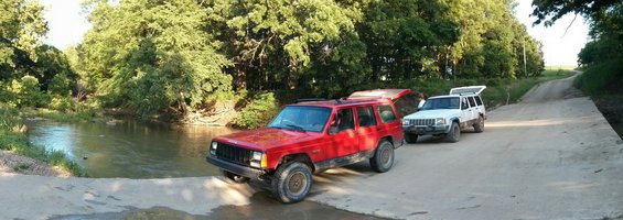 Red Jeep Cherokee XJ and white Jeep Cherokee XJ on a dirt road near a creek