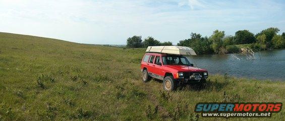 Red Jeep Cherokee with a boat on its roof rack parked by a lake