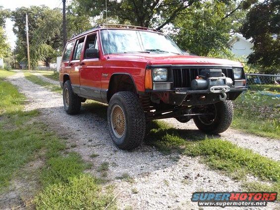 Red Jeep Cherokee XJ with a winch mounted on the front bumper, parked on a gravel driveway