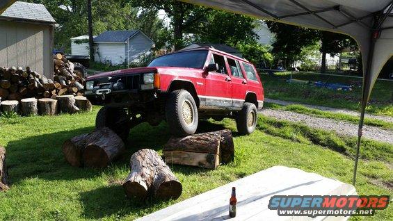 Red Jeep Cherokee XJ with front bumper winch, lifted suspension, and gold wheels