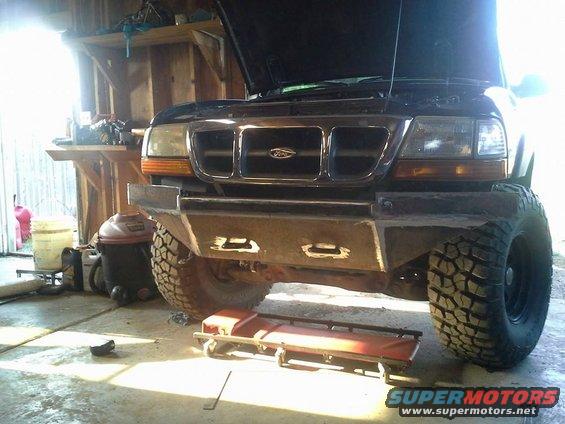 Front view of a black Ford Ranger with a custom metal bumper and large tires. The hood is open, and it's in a garage setting