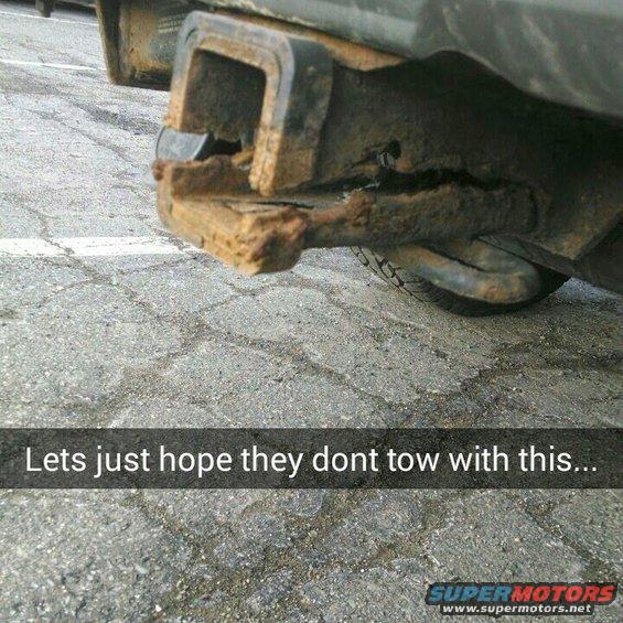 Heavily rusted trailer hitch on a vehicle, showing significant corrosion and damage