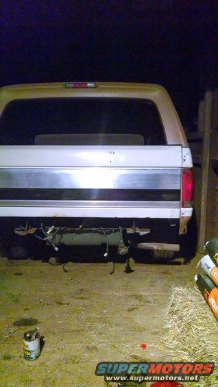 Rear of a tan and white Ford Bronco, missing its bumper and showing exposed wiring