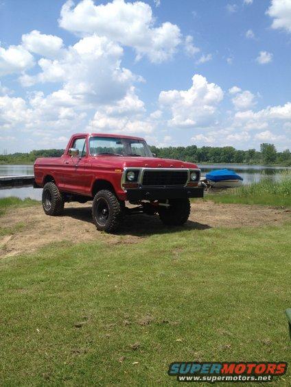 red 4x4 truck parked by a lake, blue boat on trailer behind it