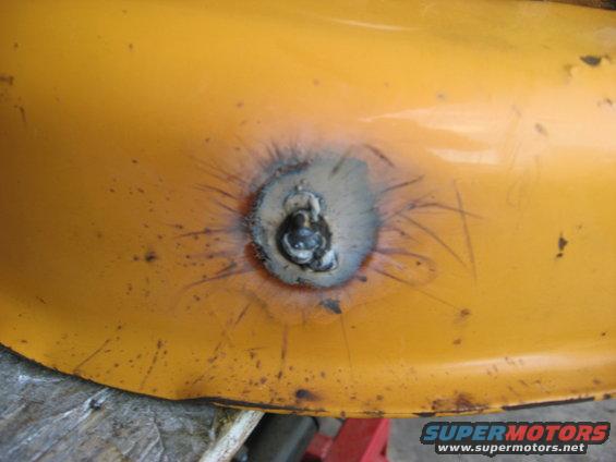 Yellow metal part with a welded bolt and surrounding scorch marks