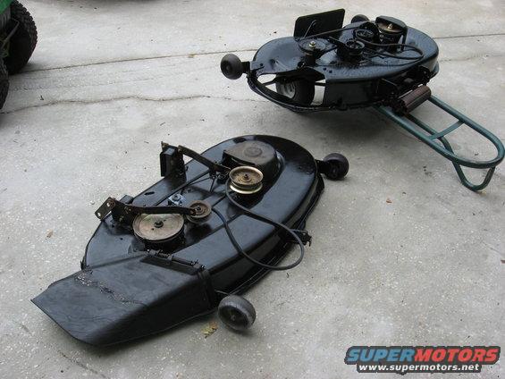 Two black mower decks with pulleys and belts on concrete
