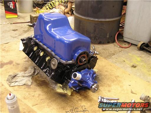 Blue painted engine block with black oil pan and blue water pump assembly on a wooden surface