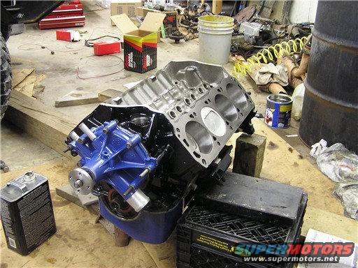Engine block and blue water pump on blocks in a garage. Tools and parts scattered around