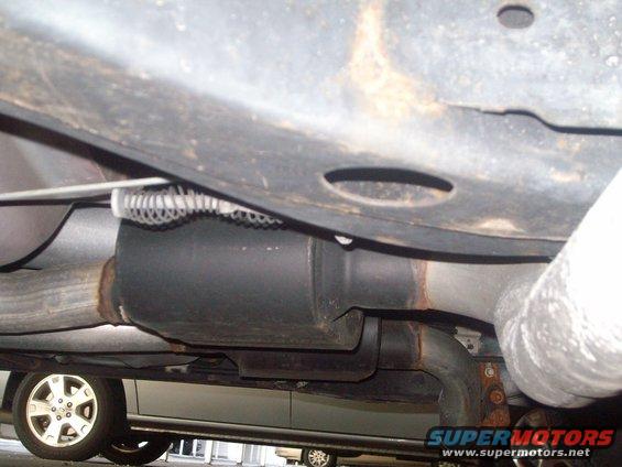 Undercarriage view showing exhaust components and a wheel. Another vehicle is partially visible below