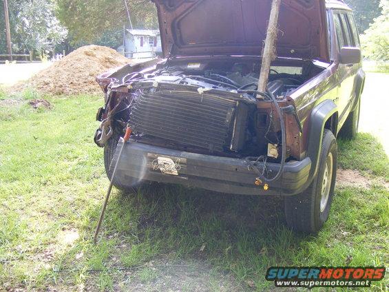 Maroon Jeep Cherokee XJ with damaged front end, hood open, and a stick propping it up