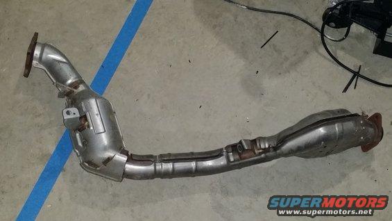 Exhaust pipe and catalytic converter assembly lying on a concrete floor with blue tape nearby