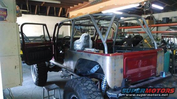 1985 Jeep CJ7 with roll cage and custom body panels, doors open, in a workshop