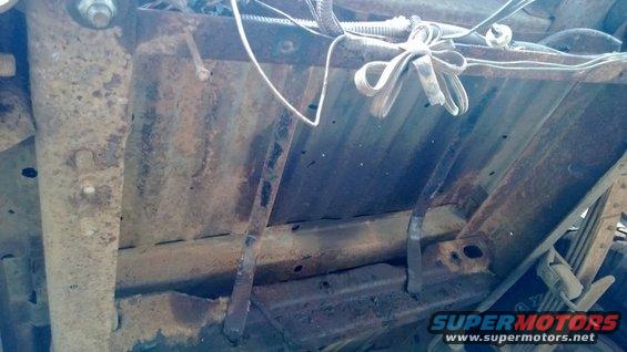 Underside view of rusty vehicle chassis with wiring and suspension parts