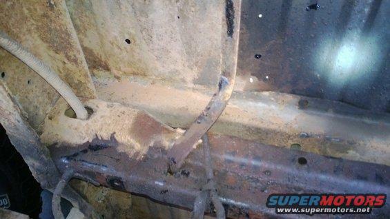 Close-up of heavily rusted vehicle frame with a wire conduit