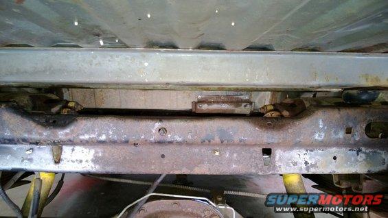 Underside of a rusty vehicle frame with yellow shock absorbers visible
