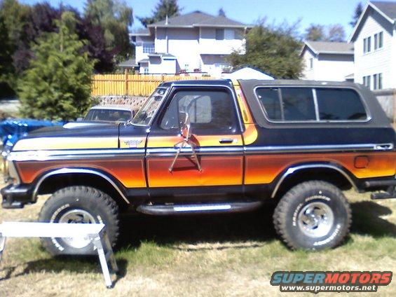 Side view of a 1978 Ford Bronco with a sunset stripe graphic. It has a black removable top and chrome side steps