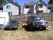 1979 Ford Bronco - A dark blue Ford Bronco and a gray sedan are parked in a grassy yard with houses in the background.