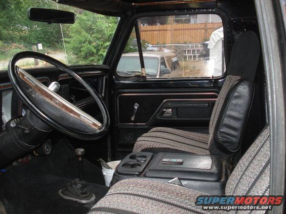Interior view of a truck's dashboard, steering wheel, and seats. A white bucket is visible on the floor