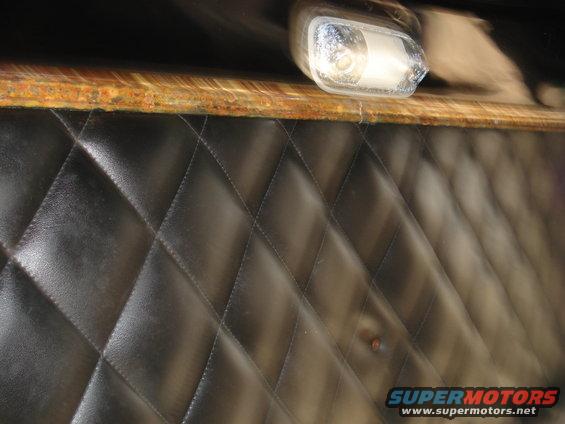 Black quilted upholstery panel with a chrome light fixture and wood trim above
