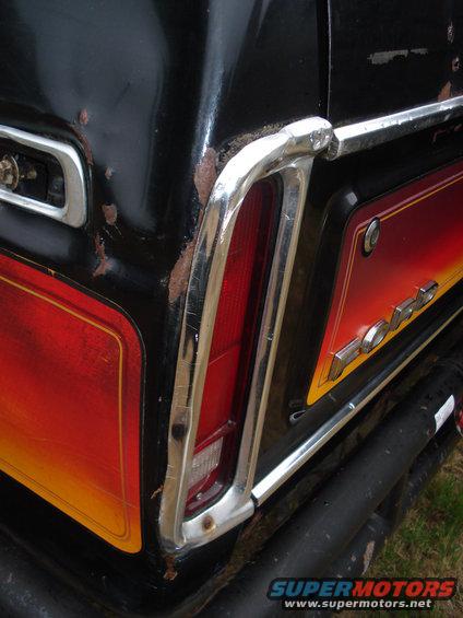 Black 1979 Ford Bronco rear corner with chrome trim, faded red and yellow stripe, and rust spots