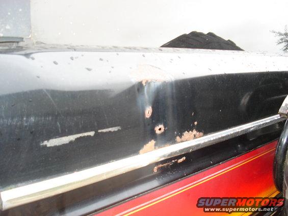 Black vehicle side with rust and dents, red and yellow stripe