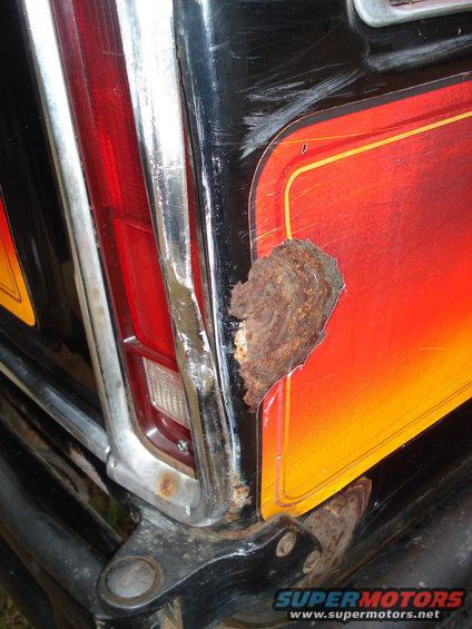 Close-up of a rusty rear fender and taillight on a black vehicle with a red and orange graphic