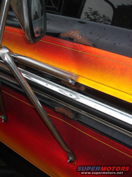 Side of a vehicle with flame paint job, showing rust spots near the door handle and trim