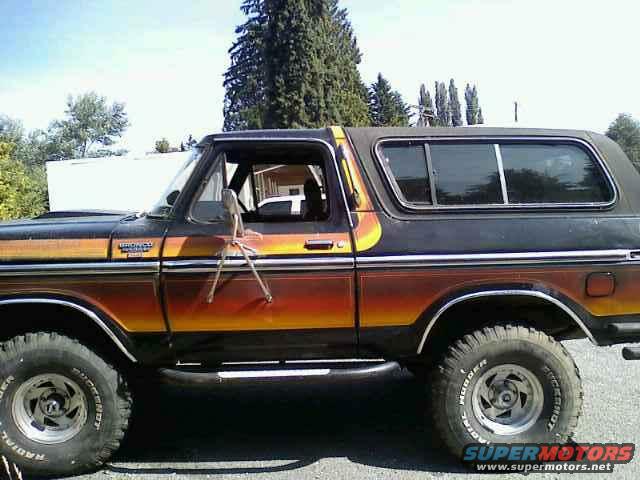 Side view of a 1978 Ford Bronco with orange and yellow gradient paint on the lower body. Chrome trim and side mirrors are visible