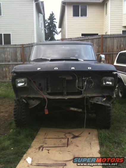 Black 1979 Ford Bronco front end with grille removed, sitting on plywood in a yard