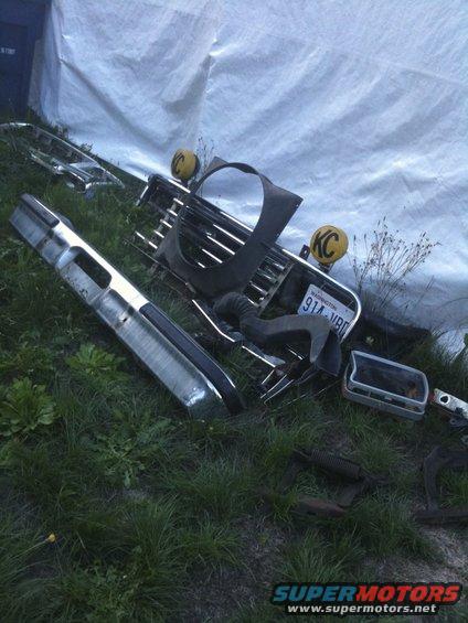 Bunch of car parts like a bumper and grille laid out on the grass