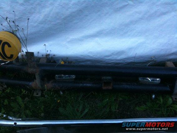 Black bumper with two rectangular lights and a trailer hitch receiver, partially covered by a tarp