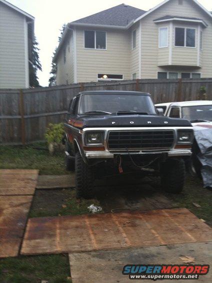 Front view of a lifted black Ford Bronco with a chrome grille and 'FORD' lettering on the hood. Another vehicle is partially visible to the right