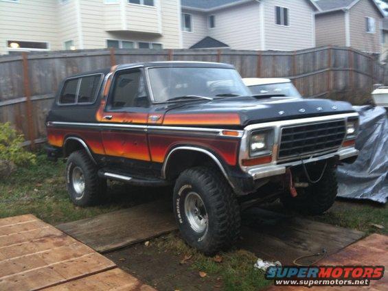Black and orange 1978 Ford Bronco with lifted suspension and off-road tires parked on wooden planks