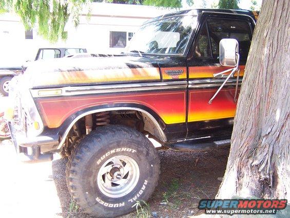 Side view of a 1979 Ford Bronco with flame graphics on the lower body. Another vehicle is partially visible behind it
