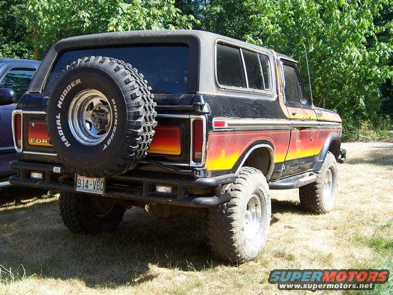 Rear view of a black Ford Bronco with a spare tire on the back. It has a red, yellow, and orange stripe on the side