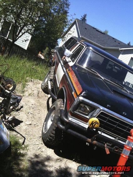 Black Ford Bronco with wood paneling and KC lights on the front bumper, parked on a dirt path