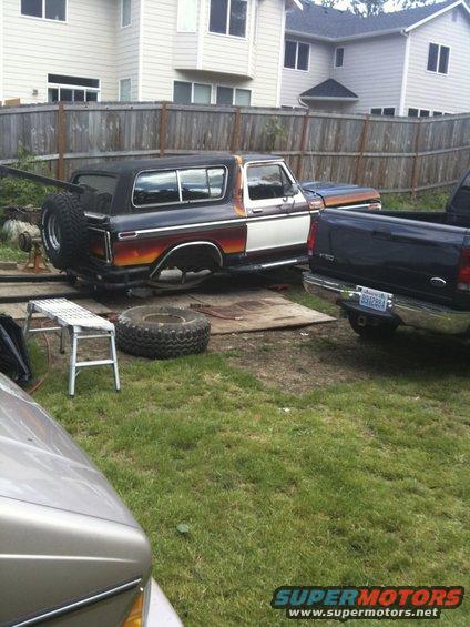 1979 Ford Bronco side view with spare tire on back, parked next to a blue pickup truck