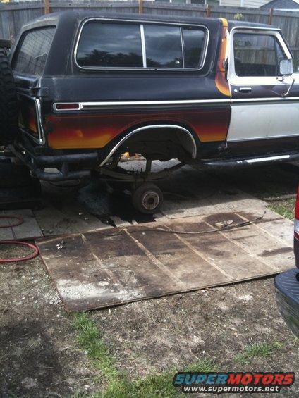 Side view of a black and white Ford Bronco with a sunset-style paint job, rear axle removed, sitting on a wooden platform