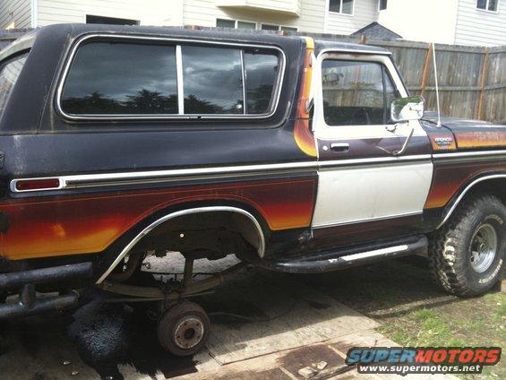 Black and white 1978 Ford Bronco with orange and yellow flame graphics, missing rear wheel