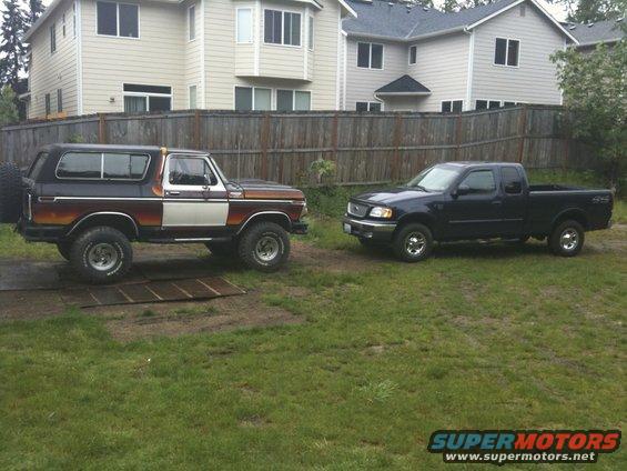 1979 Ford Bronco with two-tone paint and a spare tire on the back, parked next to a dark blue Ford F-150 pickup truck