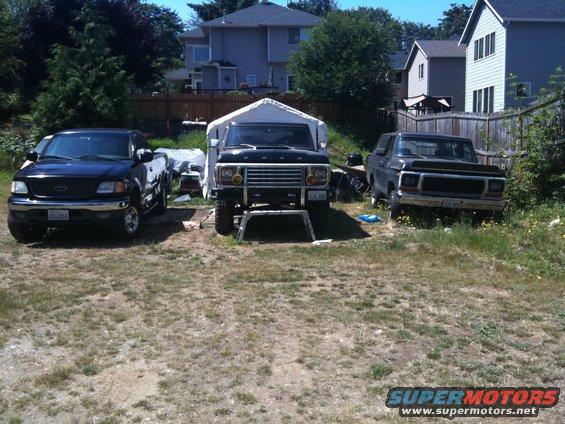 three trucks parked in a yard, one is a 1979 Ford Bronco