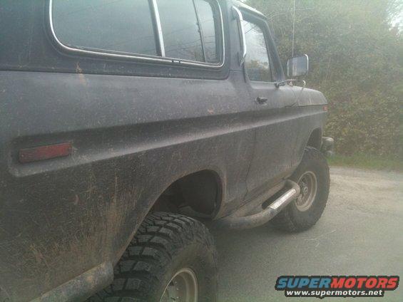 Side view of a dark-colored Ford Bronco with off-road tires and side steps. It looks like it's been driven off-road