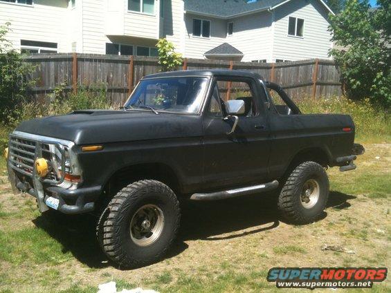 Black Ford Bronco with aftermarket bumper and roll bar, parked in a grassy yard