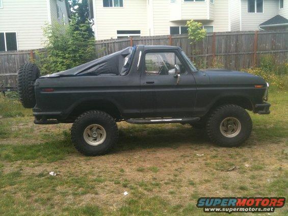 Side view of a black 1979 Ford Bronco with a spare tire on the rear and a tarp over the bed
