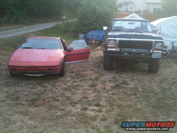 Red sports car with door open next to a black pickup truck. The truck has a license plate that reads C14-300