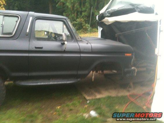 Black Ford Bronco with a matte finish, side view, parked outdoors under a tarp