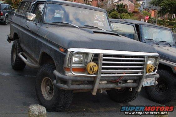 Black Ford Bronco with KC lights on the front bumper, parked next to a dark colored Jeep