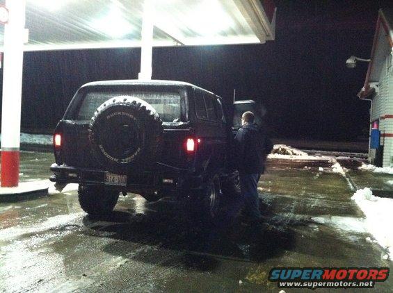 Black 1978 Ford Bronco with spare tire on rear door, parked at gas station at night