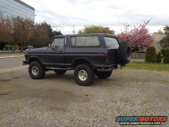 Dark SUV with spare tire mounted on the back, parked on gravel